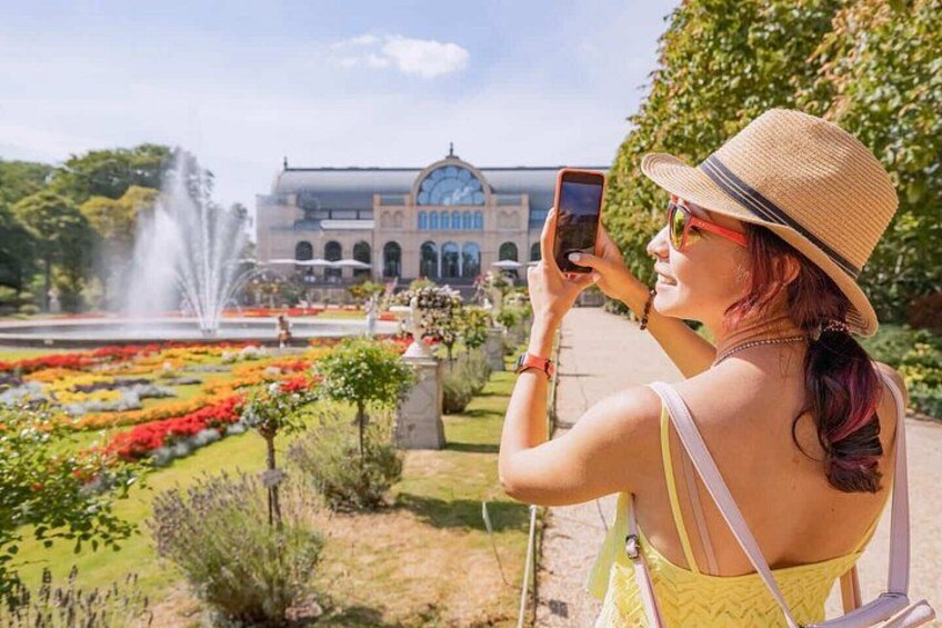 Una donna fotografa un giardino con una fontana e un edificio sullo sfondo. 2