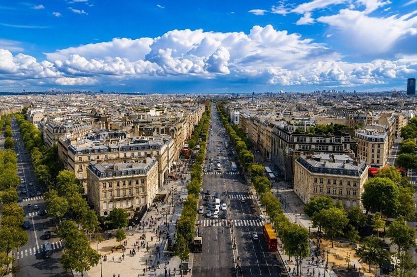 A cityscape with a wide avenue lined with historic buildings, a clear sky, and distant city skyline. 1