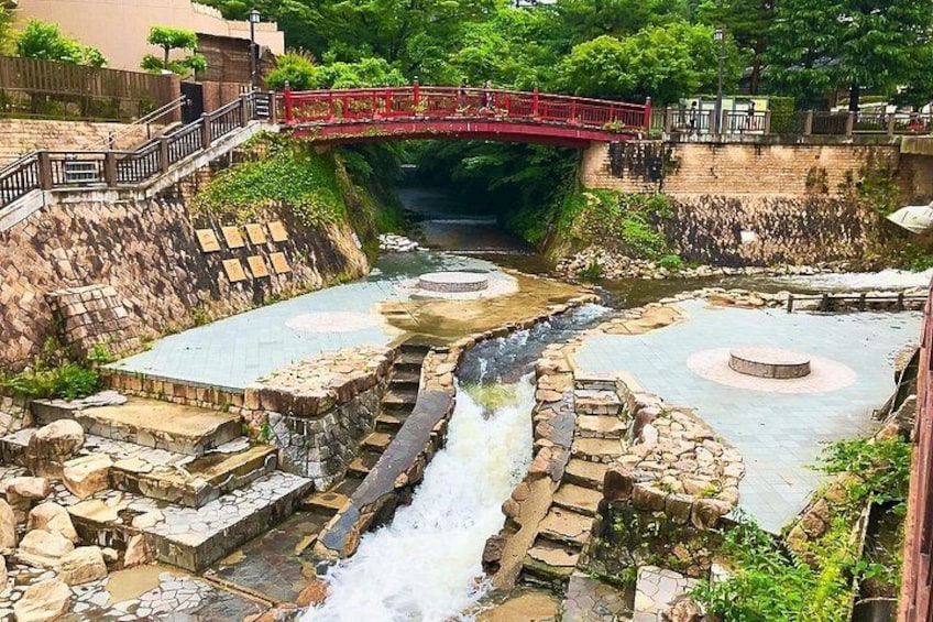 Un canal d’eau en pierre, surmonté d’un pont rouge, entouré de verdure et bordé d’escaliers en pierre. 5