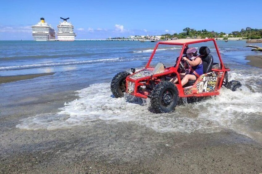 A red off-road vehicle on a beach with waves, a cruise ship in the background, and a clear sky. 5