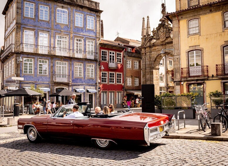 A vintage red convertible car driving down a cobblestone street lined with colorful buildings. 5