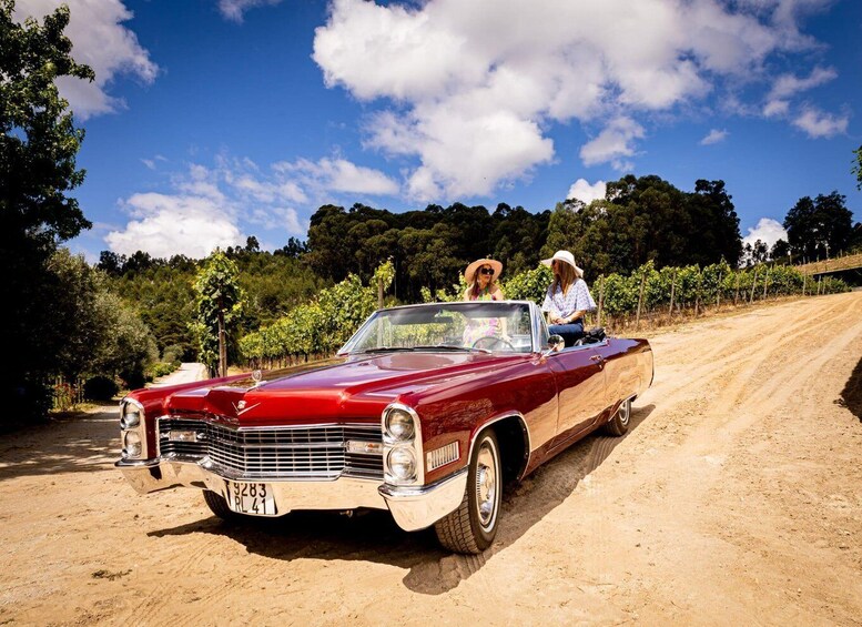 A vintage red convertible car parked on a dirt road with two people sitting in the front. 3
