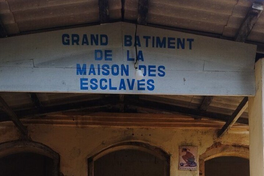 Un cartello con la scritta 'GRAND BATIMENT DE LA MAISON DES ESCLAVES' su un edificio storico. 3