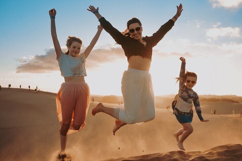 Three people jumping in the air on a sandy beach with a clear sky. 1