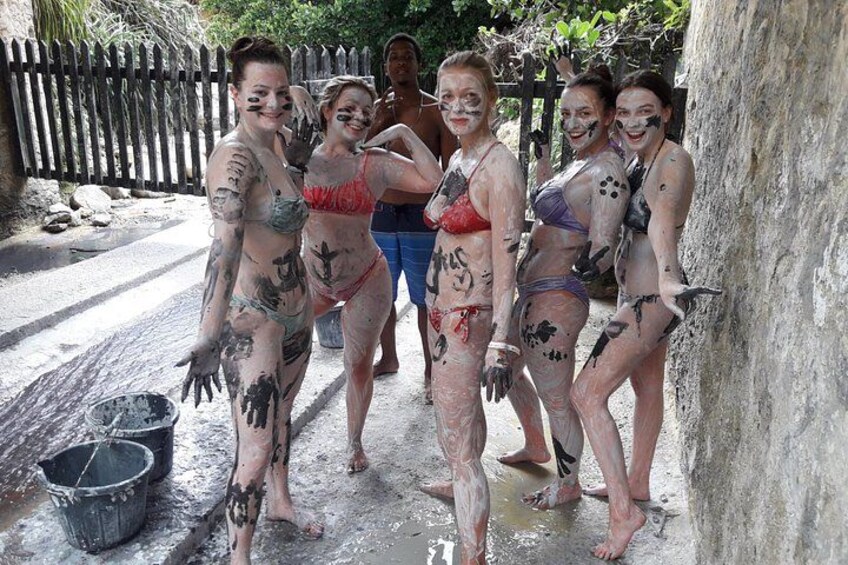 Mensen in bikini's, overdekt met zwarte verf, staan op een nat oppervlak met emmers in de buurt. 3