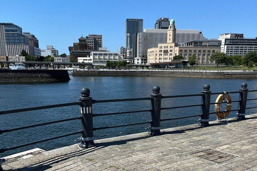 A waterfront cityscape with modern buildings, a river, and a pedestrian walkway with balustrades. 3