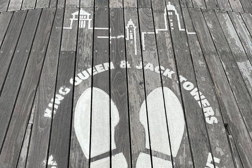 A wooden deck with a white painted design featuring the text 'KING QUEEN & JACK TOWERS' and a silhouette of a building. 2