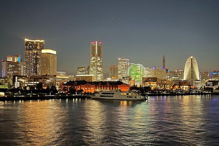 A city skyline at night with illuminated buildings, a Ferris wheel, and a boat on the water. 1
