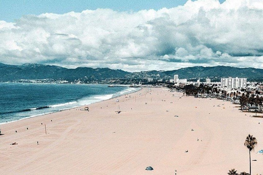 A wide beach with a clear sky, mountains in the background, and a few buildings along the shore. 5
