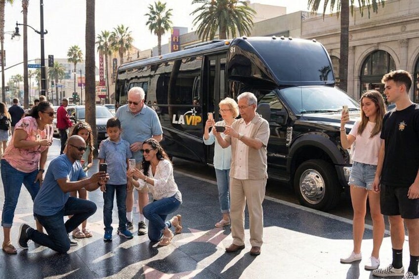 A group of people taking photos with a black bus labeled 'LAVIP' in a city street with palm trees and buildings in the background. 3