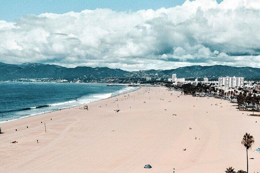 A wide beach with a clear sky, mountains in the background, and buildings along the coastline. 4