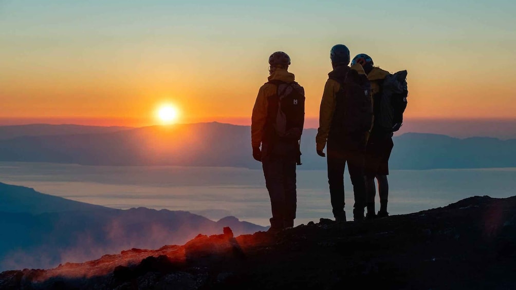 Three people standing on a mountain peak during sunset. 5