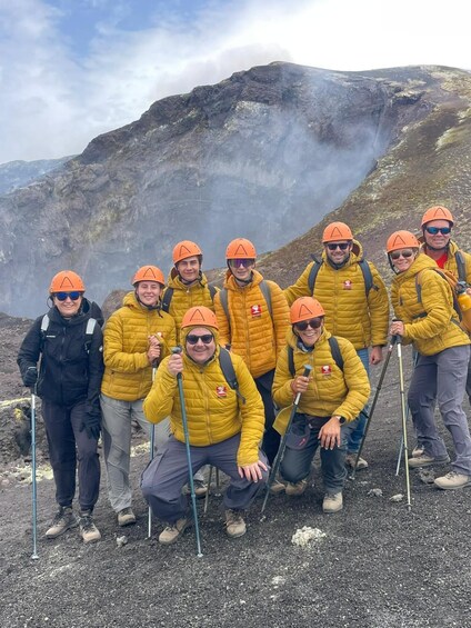 A group of people in yellow jackets and orange helmets posing on a rocky mountain. 4