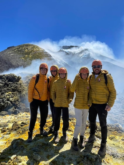 A group of people standing on a rocky terrain with a mountain and steam in the background. 2