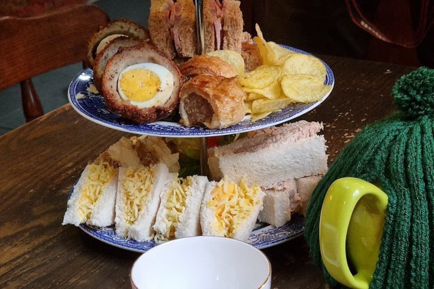 A three-tiered plate with sandwiches, a boiled egg, and chips. 2