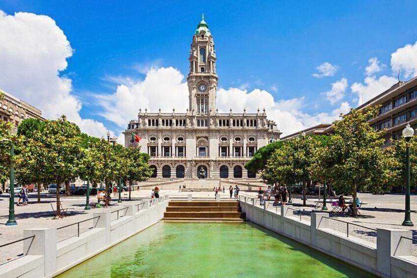 A historic building with a clock tower, surrounded by a plaza with a fountain and trees. 3