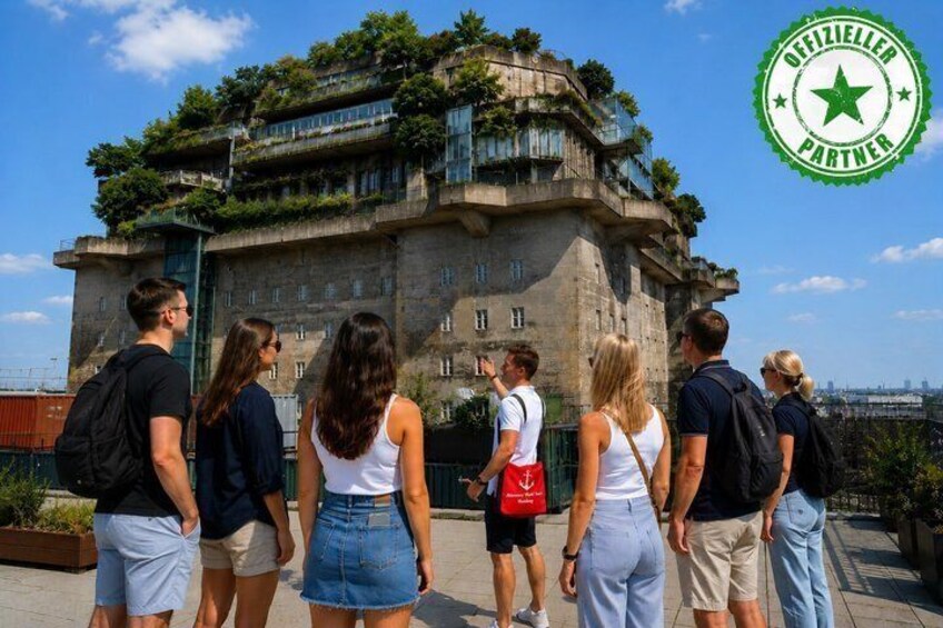 A group of people standing in front of a historic building with a green roof and a star emblem in the corner. 1