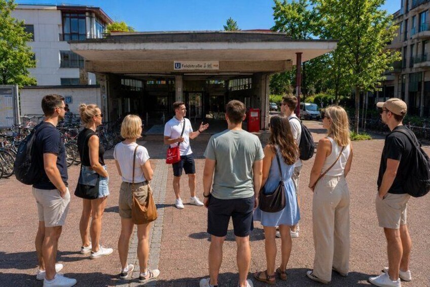 A group of people standing in front of a building with a sign that reads 'Feldstraße 4.' 2