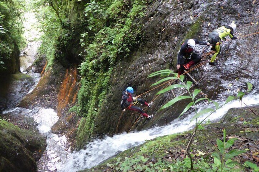 Two people rappelling down a rocky cliff with a flowing stream below. 4