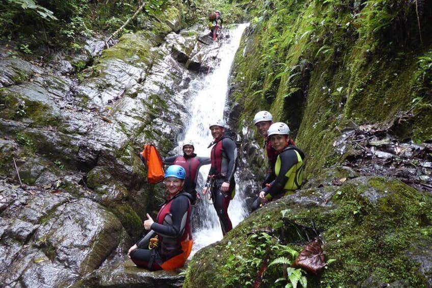 A group of people in helmets and life jackets near a waterfall in a forested area. 2