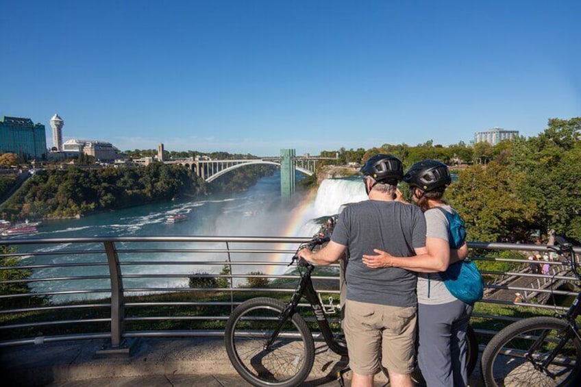 A couple standing by a railing overlooking a waterfall and a rainbow. 1
