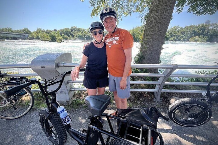 Two people standing by a river with a bicycle and a grill. 4