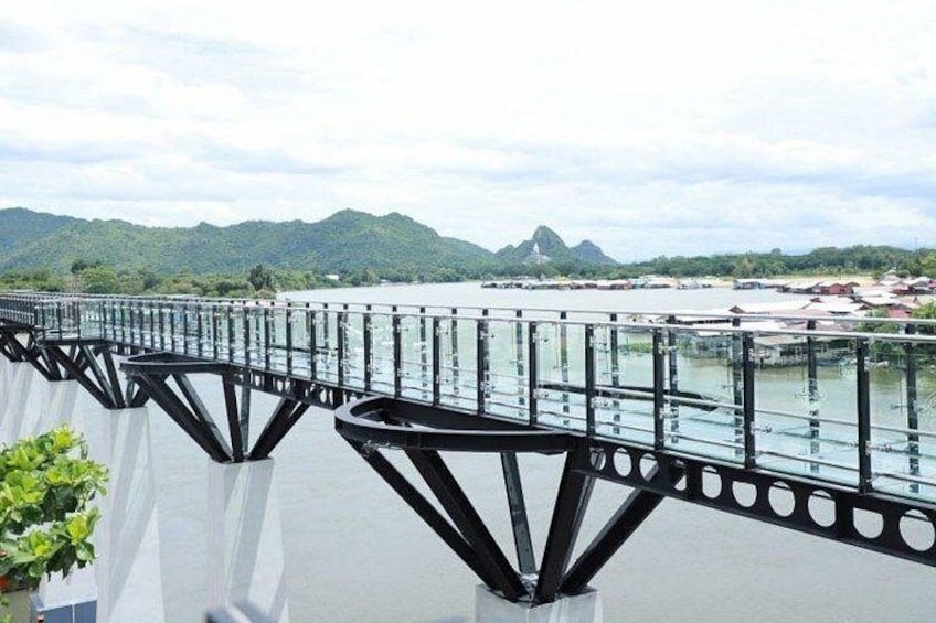 A bridge with a metal framework and glass railing, overlooking a body of water and distant mountains. 2