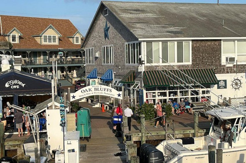 A waterfront area with a cafe, a boat docked at the pier, and a building with a sign reading 'Oak Bluffs.' 4