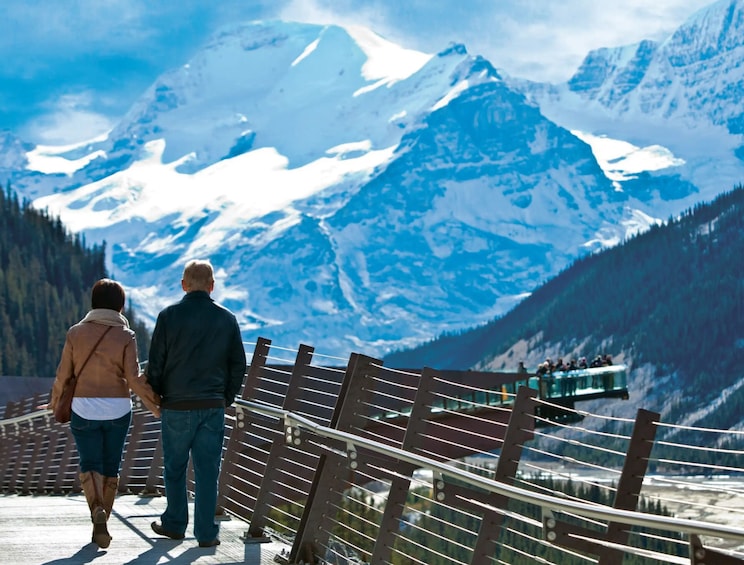 A couple walking on a wooden bridge with a mountain backdrop. 3