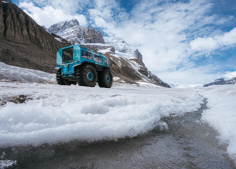 A blue vehicle on a snowy landscape with mountains in the background. 4