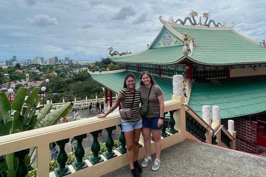A traditional building with a green roof and ornate decorations, a railing with decorative posts, and a cityscape in the background. 1