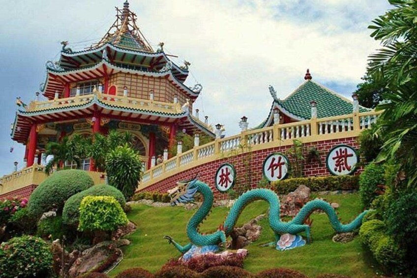 A traditional Chinese pagoda with ornate architecture, a landscaped garden with a large dragon sculpture, and Chinese characters on the walls. 2
