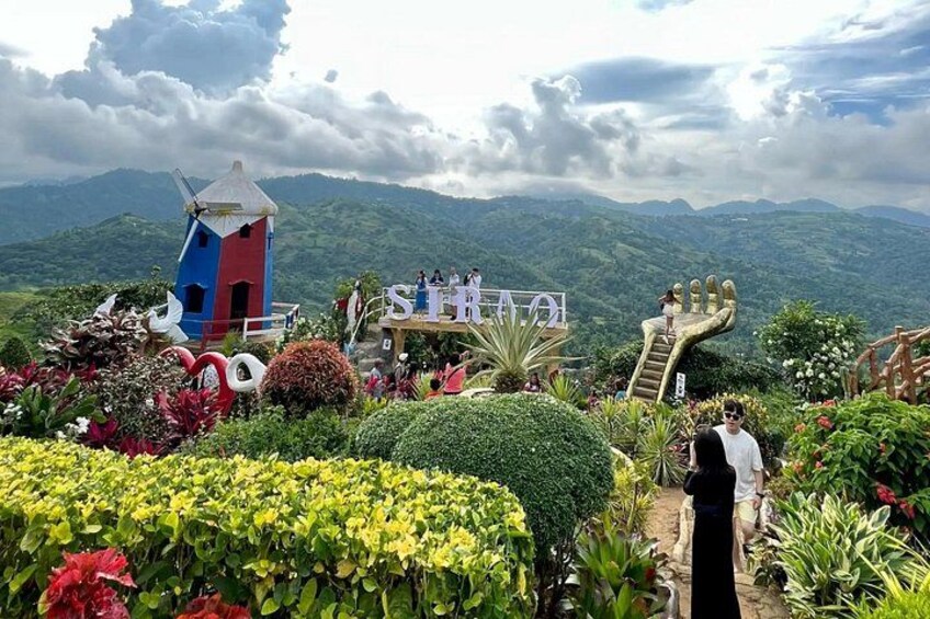 A colorful garden with a windmill, a hand-shaped sculpture, and a building with people on a platform. 3