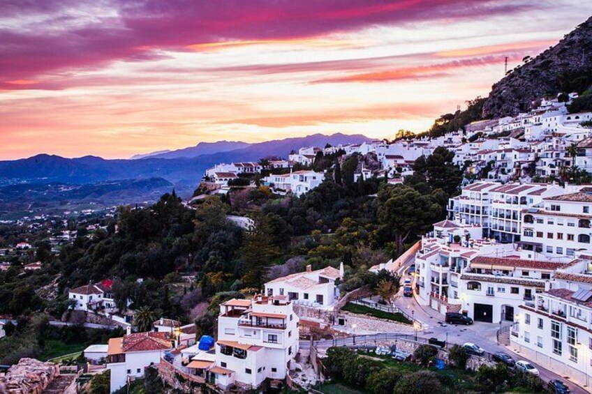 A coastal town with white buildings, a sunset, and mountains in the background. 2