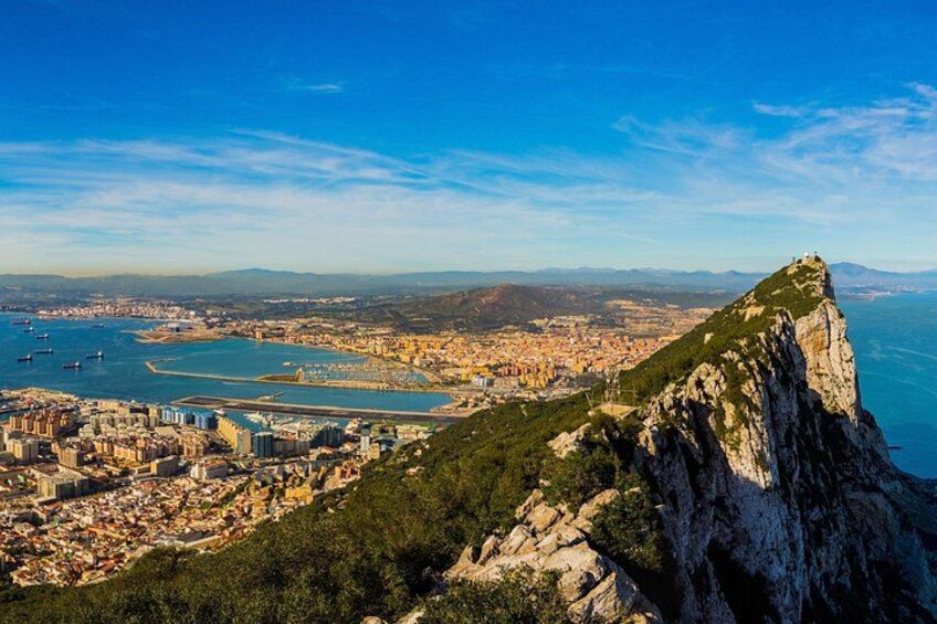 A coastal city with a prominent cliff, a harbor, and a distant mountain range. 2