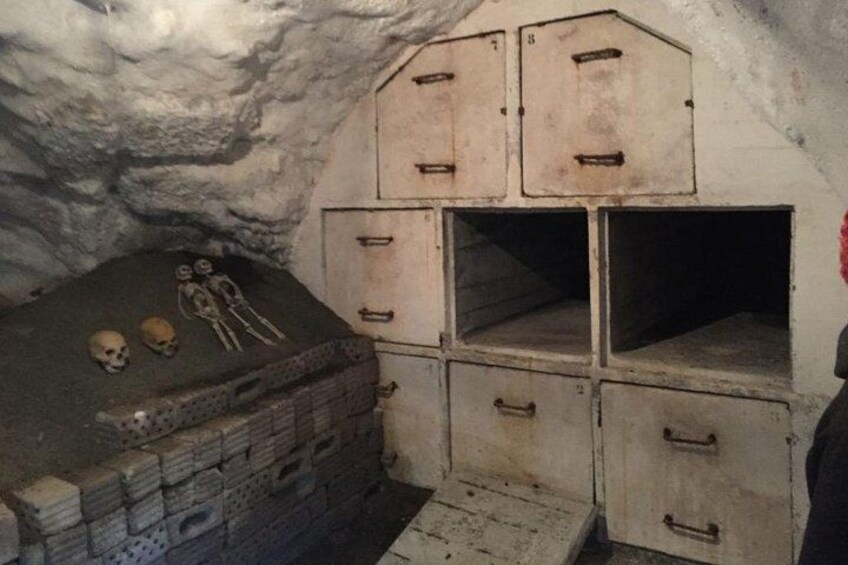 A cave with a stone wall, a wooden chest, and two skeletons. 4