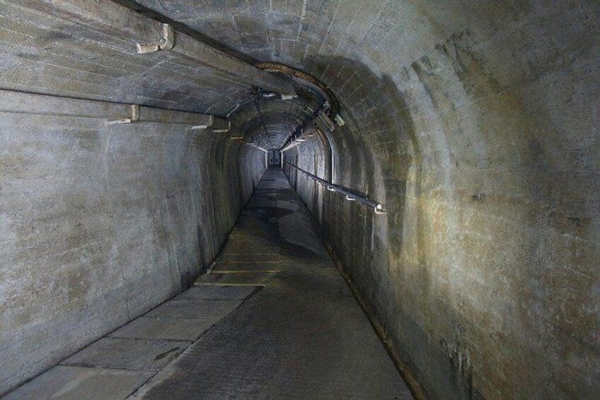 A tunnel with concrete walls, a metal railing, and a concrete floor. 5