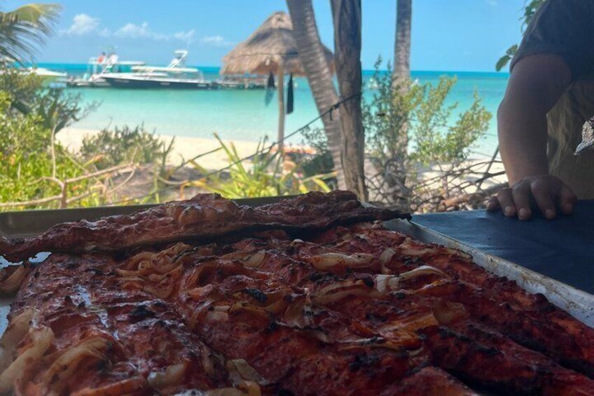 A grill with grilled meat and a view of a beach with palm trees and a boat. 3