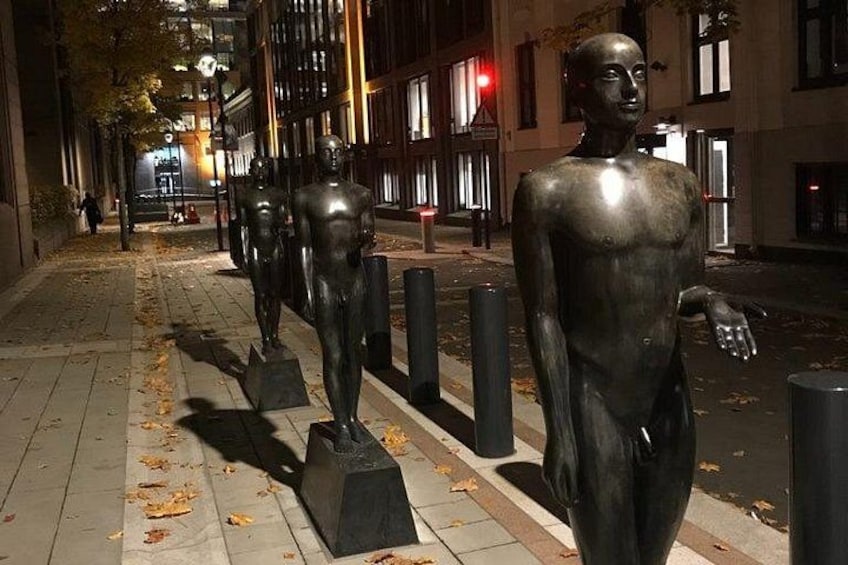 Une rangée de statues en bronze, alignées sur un trottoir de la ville, la nuit. 2