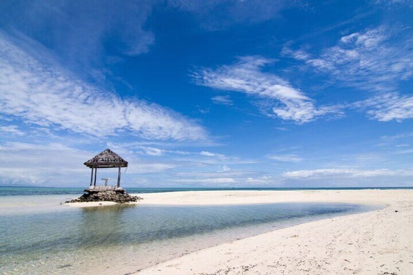 A beach with a small hut on a sandy islet, clear blue sky, and calm sea. 2