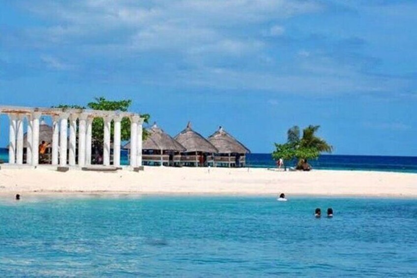 A beach with a gazebo, overwater bungalows, and swimmers in the water. 4