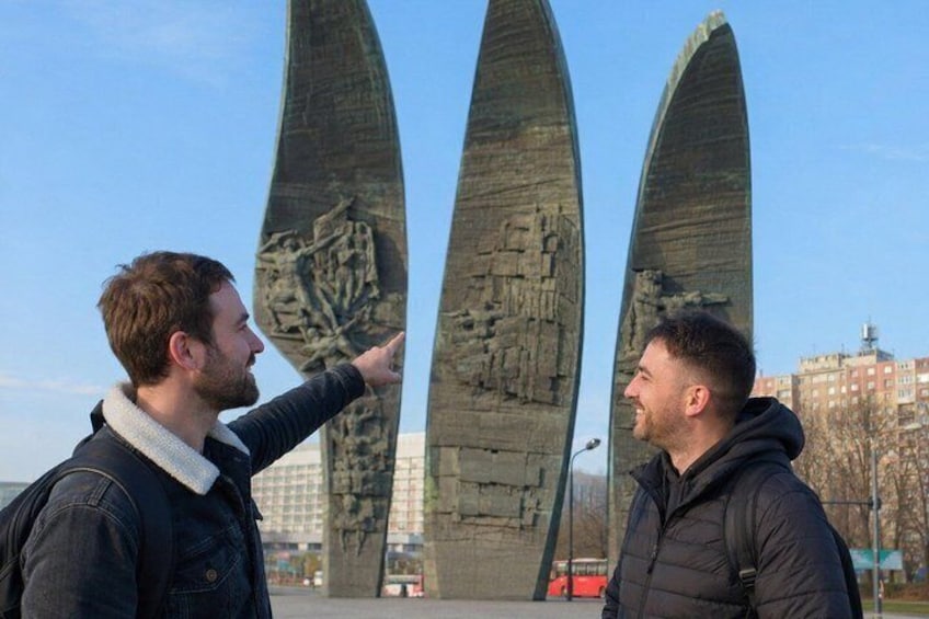 Twee personen staan voor een monument met drie hoge, puntige constructies. 2