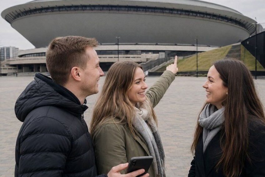 Drie personen staan voor een modern gebouw met een opvallend, circulair ontwerp. 4