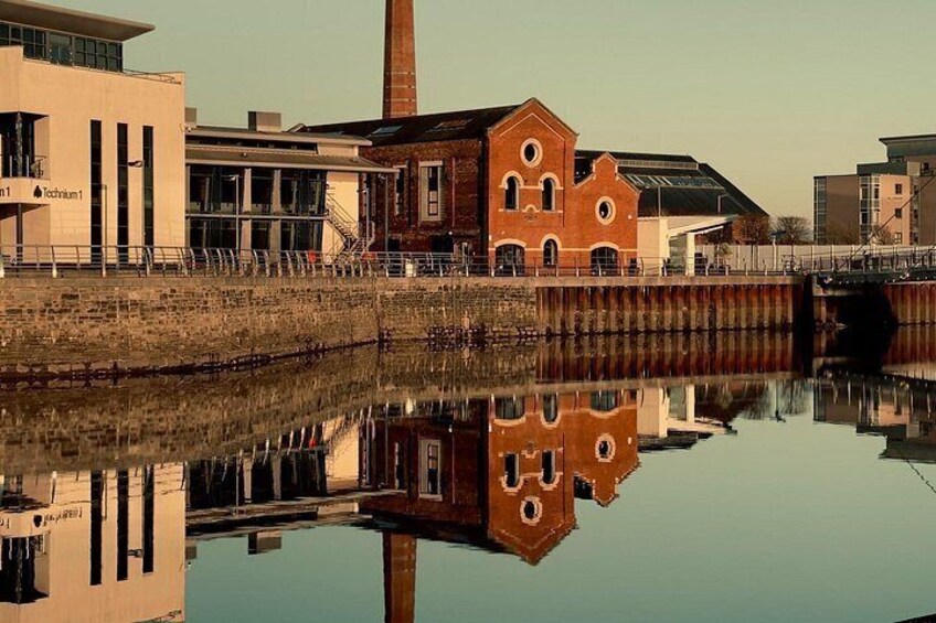 Een rivier die gebouwen weerspiegelt, waaronder een bakstenen gebouw met ronde ramen en een modern gebouw met verticale lijnen. 3