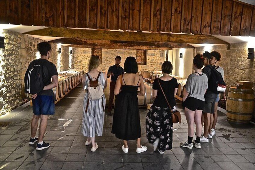 A group of people standing in a wine cellar with wooden beams and stone walls. 1