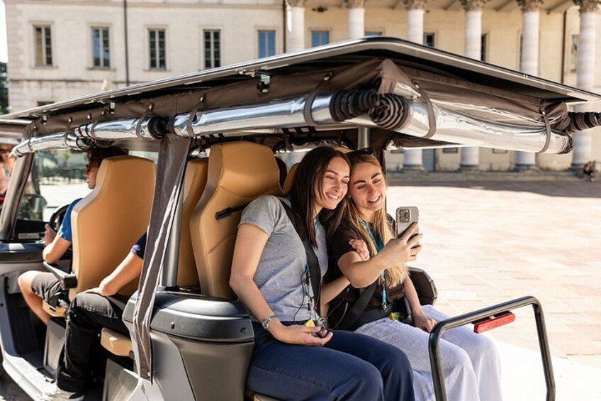 Un vehículo descapotable con techo, pasajeros tomándose un selfie y arquitectura clásica al fondo. 4
