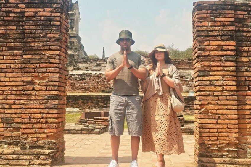 A man and woman standing between ancient brick structures, possibly ruins, with a historical site in the background. 3