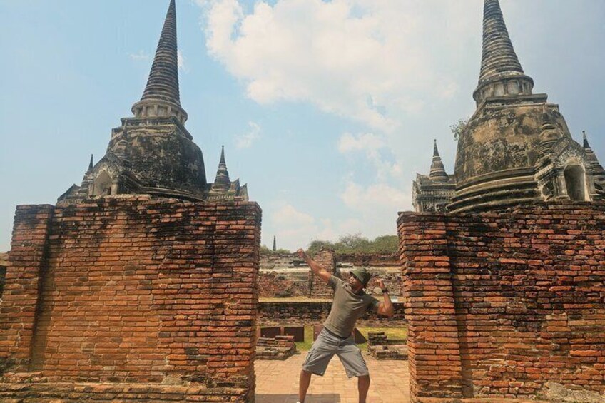 A person taking a photo with a historic brick structure and pointed towers in the background. 1