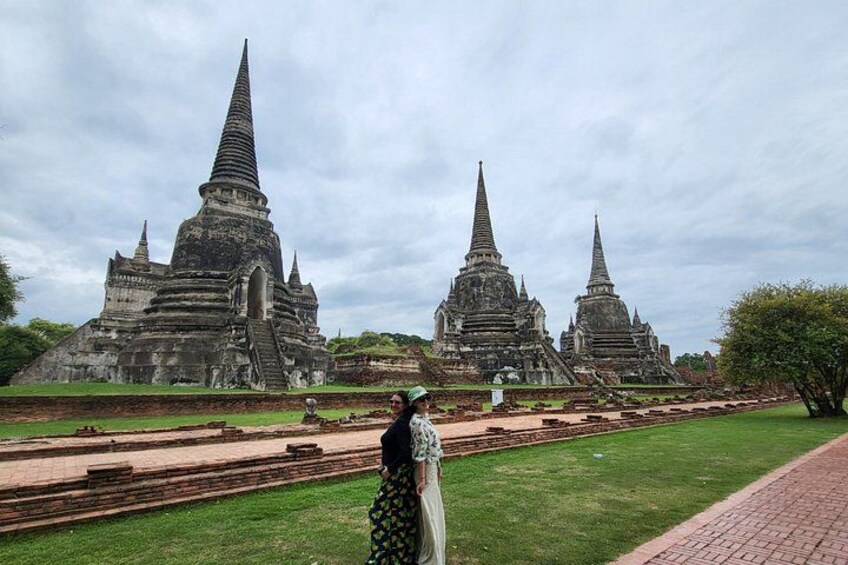 Ancient temple ruins with multiple structures, a grassy foreground, and a cloudy sky. 2