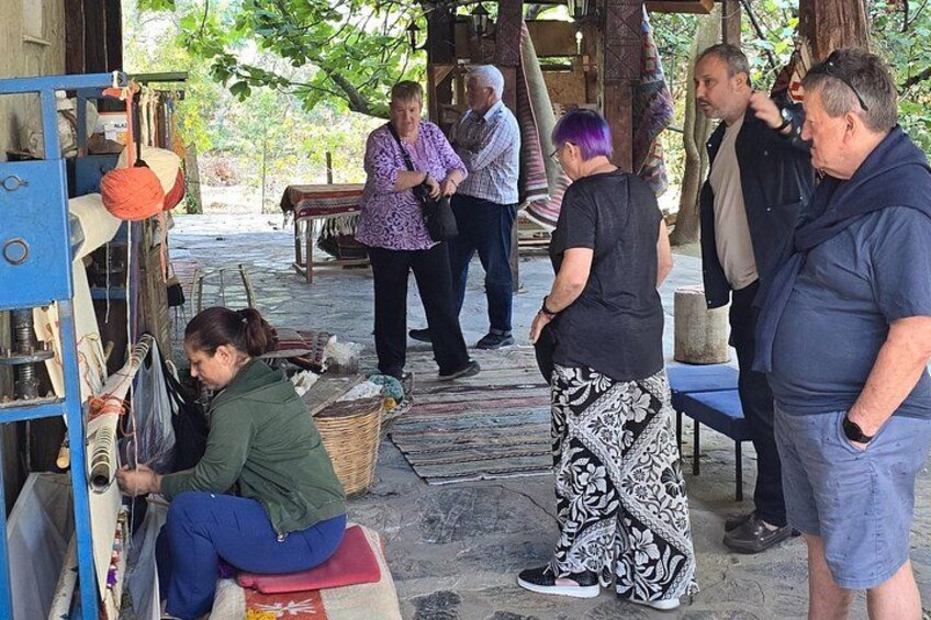 A group of people in an outdoor setting with a blue structure, possibly a market stall, and a person seated on a stool working on a sewing machine. 5
